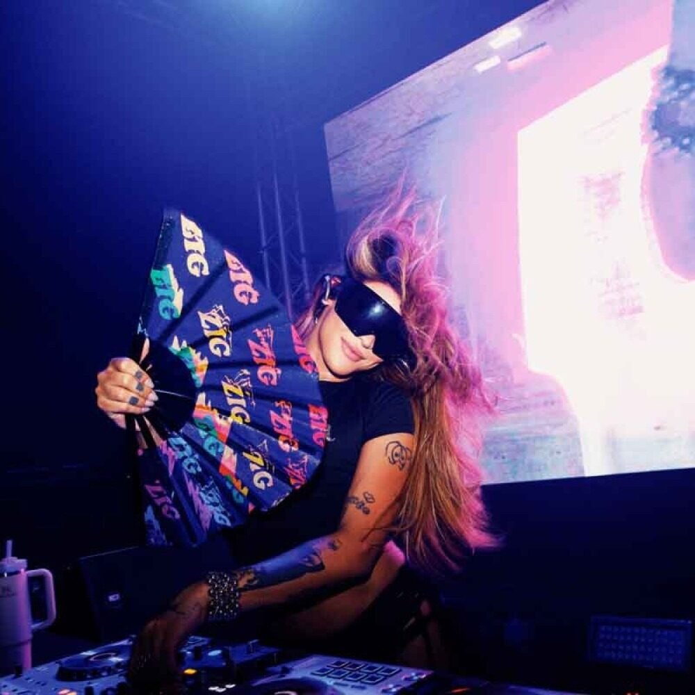 Cantora com óculos escuros e leque colorido se apresenta em palco com iluminação rosa