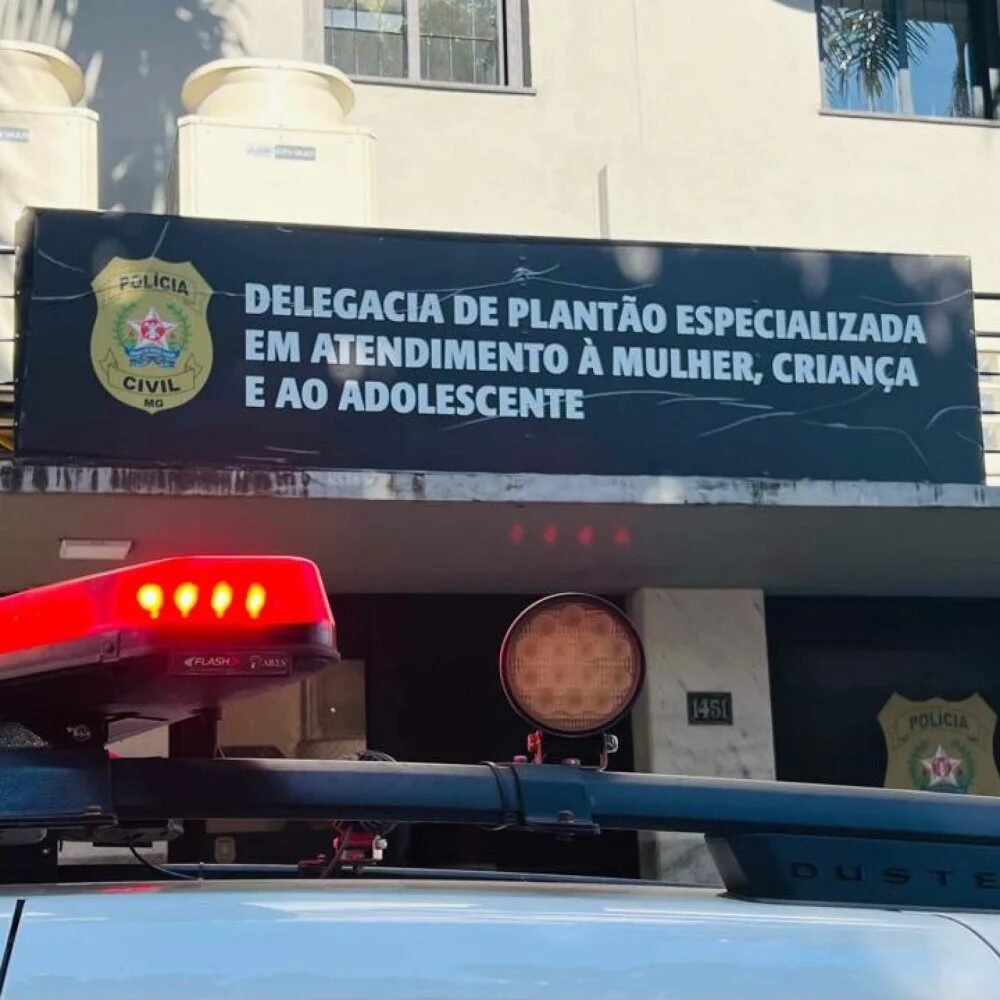 Placa da Delegacia de Plantao Especializada em Atendimento a Mulher com viatura policial em primeiro plano