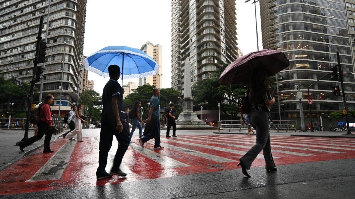 Pedestres com guarda-chuvas atravessam rua com piso molhado em Belo Horizonte