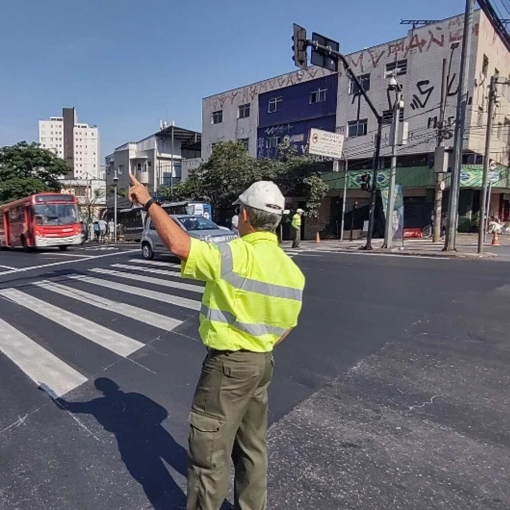 Agente de trânsito de colete refletivo orienta o fluxo em cruzamento com ônibus ao fundo em Belo Horizonte