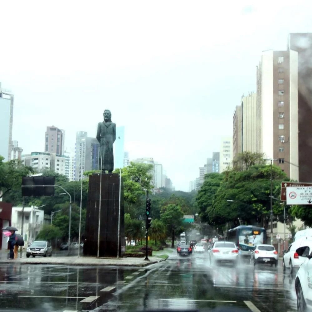 Dia chuvoso em Belo Horizonte com trânsito de carros na rua molhada e a estátua de Tiradentes ao fundo