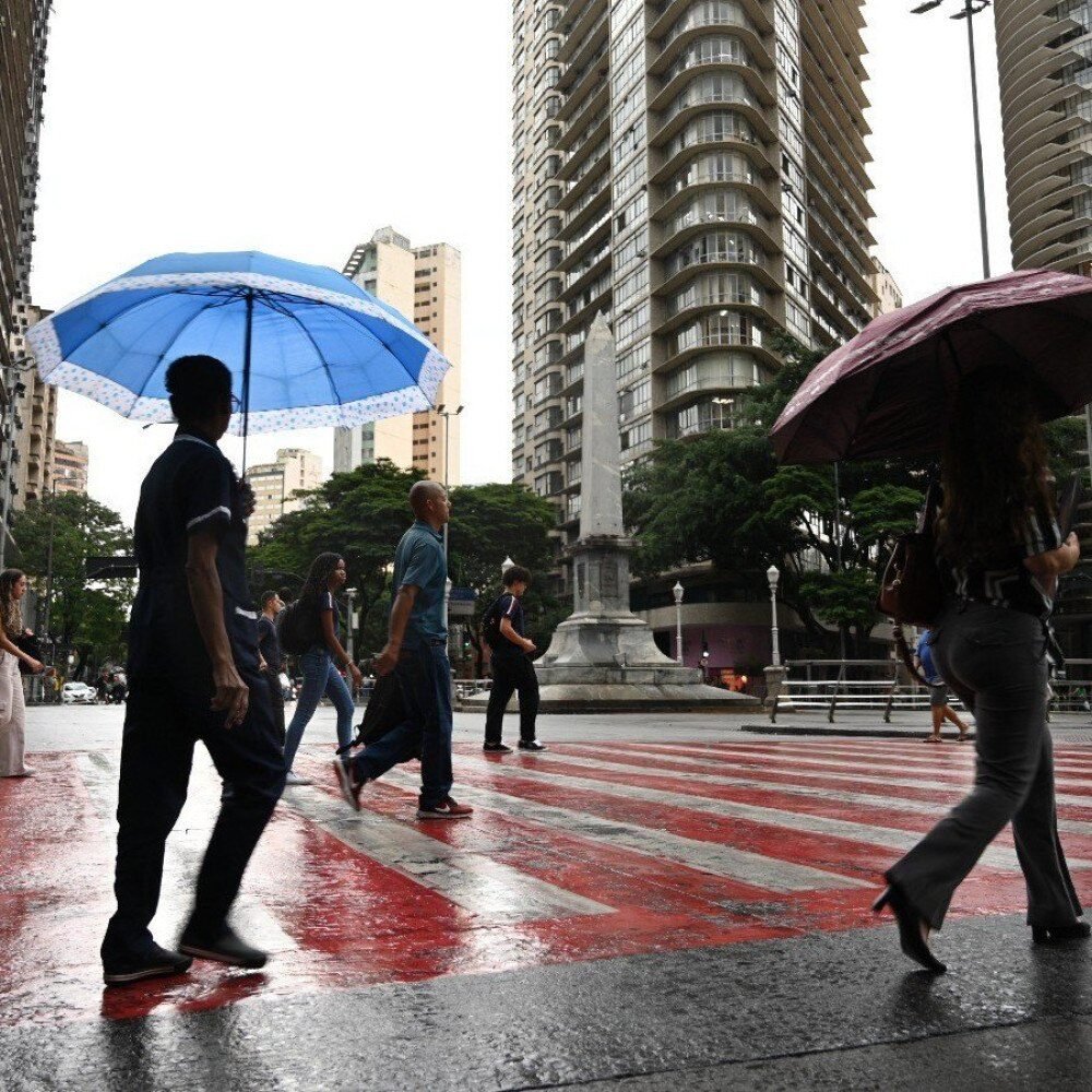 Pedestres com guarda-chuva cruzam rua molhada na Praça Sete em Belo Horizonte